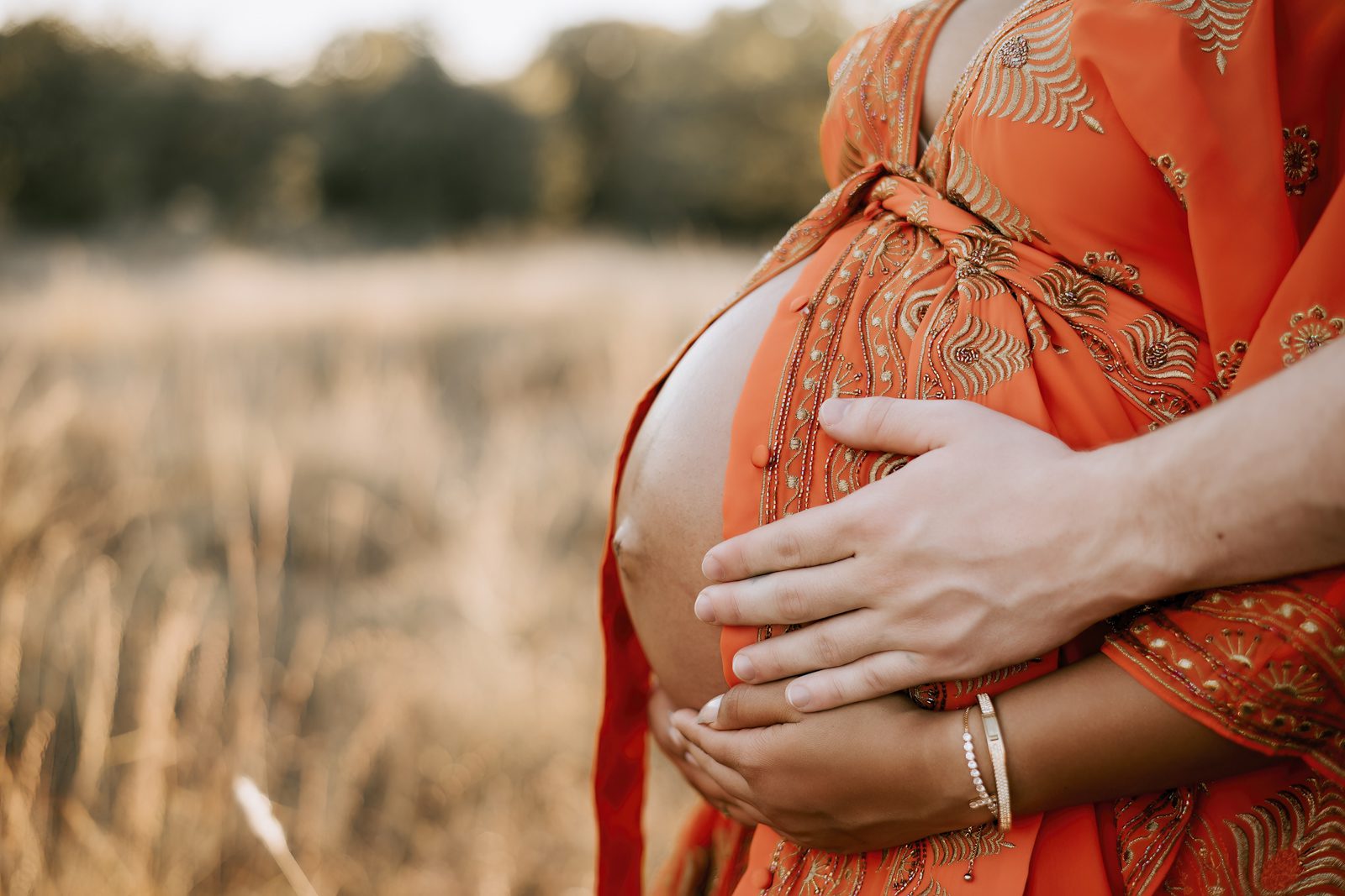 A pregnant woman holding her husband's hand in a field during outdoor maternity photography.