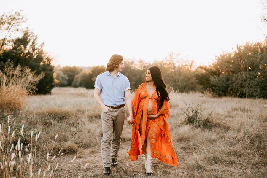 maternity-couple-walking-side-by-side-holding-hands-in-front-of-beautiful-sunset