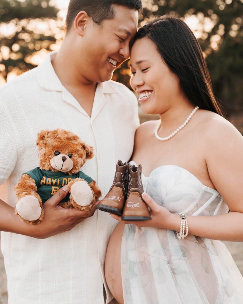 Expecting Couple Holding Baby Shoes And Teddy Bear During Maternity Photography Session Outdoors