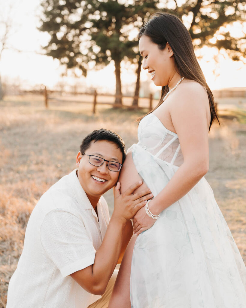 What To Wear For A Summer Maternity Session 6 Father Smiling While Holding Pregnant Belly During Outdoor Maternity Photography Session