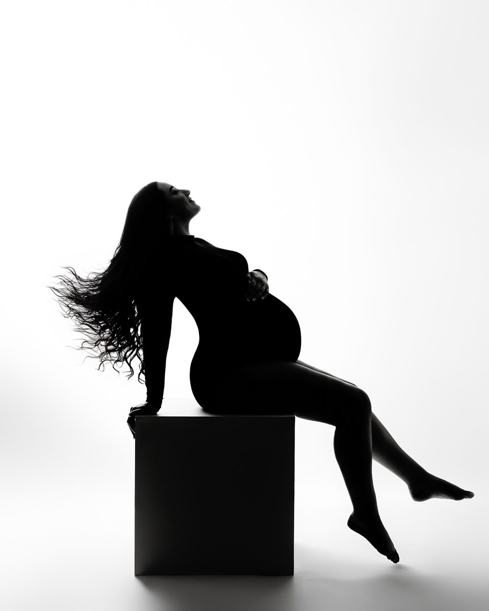 A silhouette of a pregnant woman sitting on a box.
