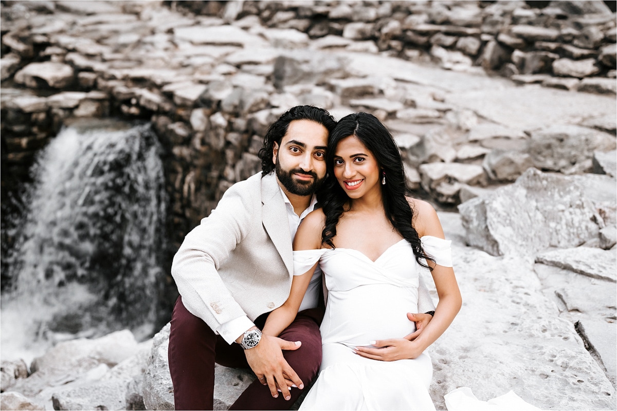 Expecting Couple Sitting On Large Rocks Looking At Camera Smiling For Dallas Maternity Photography