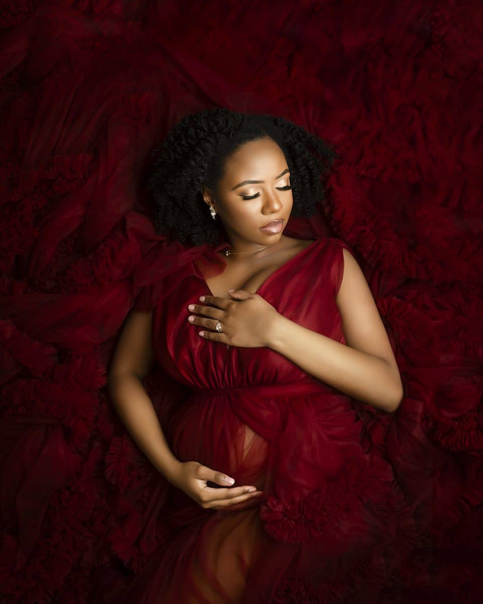 A pregnant woman draped in a red gown gently touching her belly for her dream maternity photoshoot