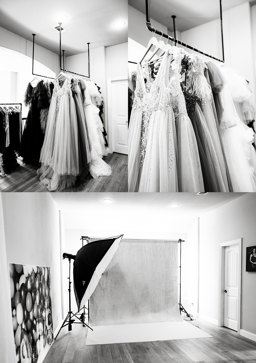 A Black And White Image Showing A Collection Of Elegant Gowns On Hangers Within A Studio Setup, Complete With A Backdrop And Professional Lighting Equipment.