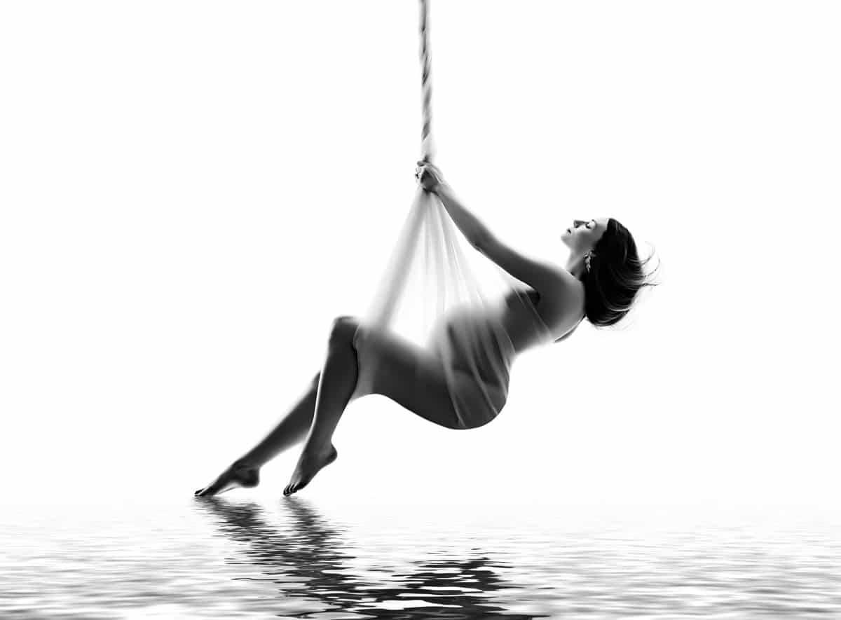 A person suspended in the air by a rope, with water beneath them and a bright white background.