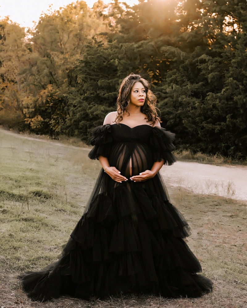 Pregnant Woman Wearing A Black Dress Cradles Her Pregnant Belly For Maternity Shoot Dallas 