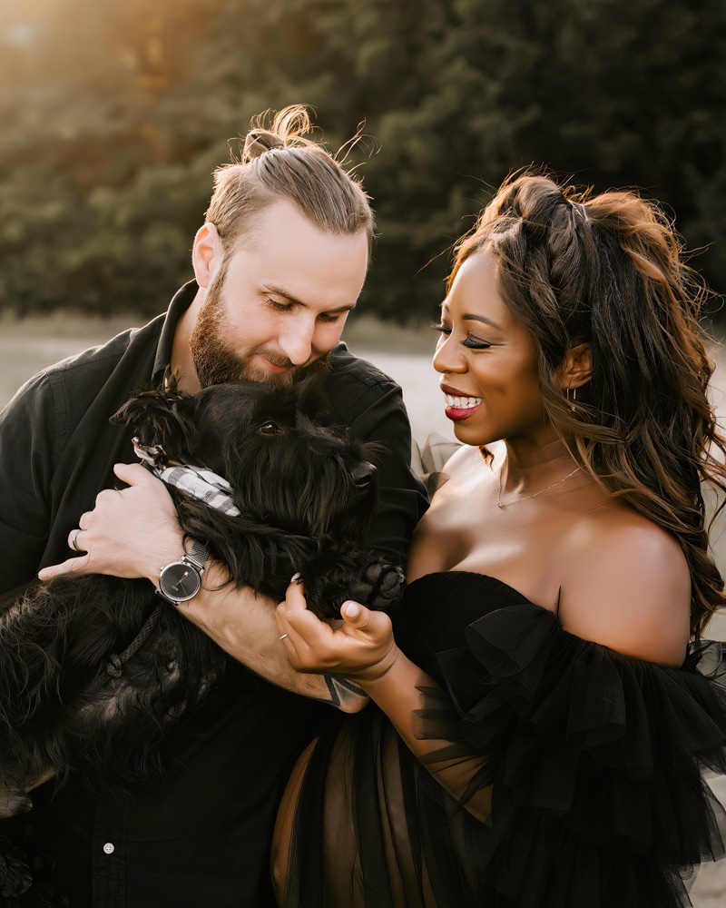 Pregnant Couple Outdoors Smiling And Looking At The Their Dog For A Maternity Photoshoot In Dallas