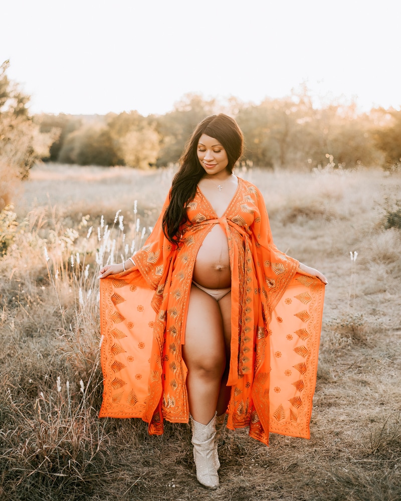 Pregnant woman in flowing orange dress during golden hour outdoor maternity photoshoot in Dallas