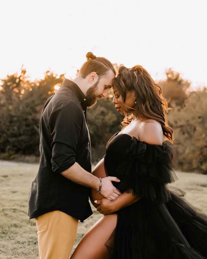 Couple Stands Close In An Outdoor Setting Smiling At Each Other During A Dallas Maternity Photoshoot