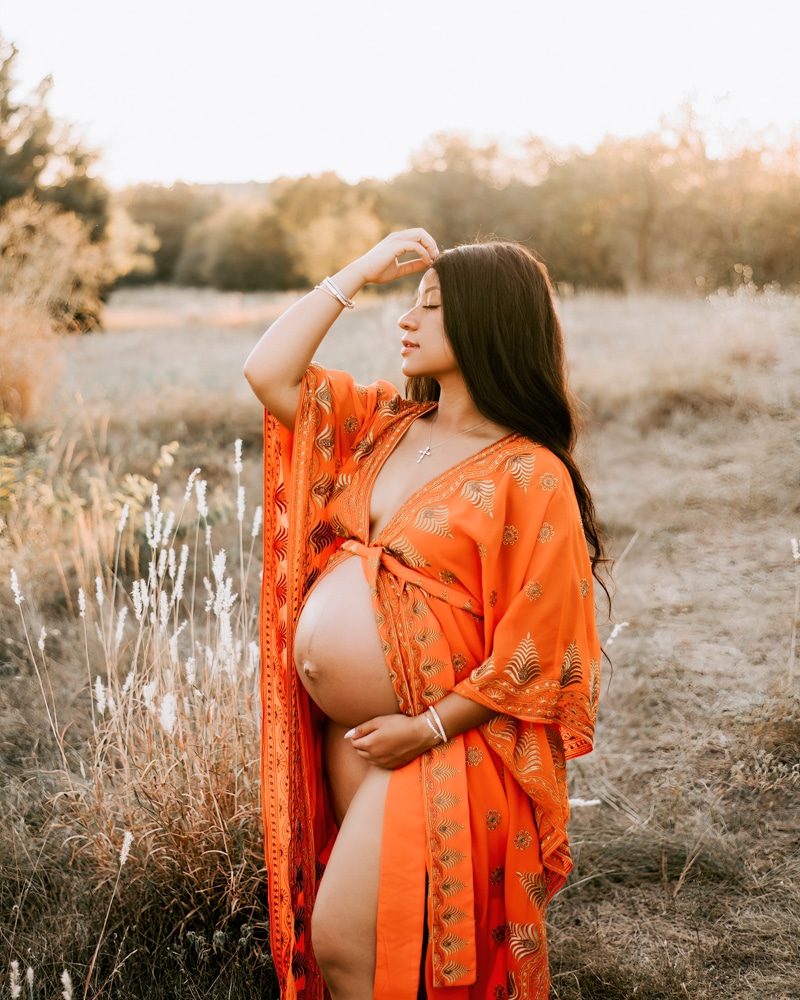 expecting woman in orange boho gown holding her baby bump during golden hour maternity photoshoot in dallas