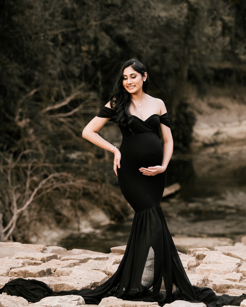 Pregnant Woman Wearing Black Fitted Gown Posing Near Rocks For Dallas Maternity Photographer