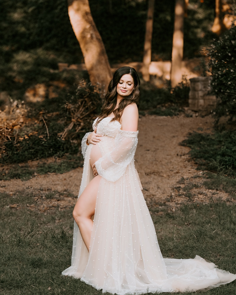Pregnant Woman Posed In A Park Smiling At Camera For A Professional Maternity Photographer