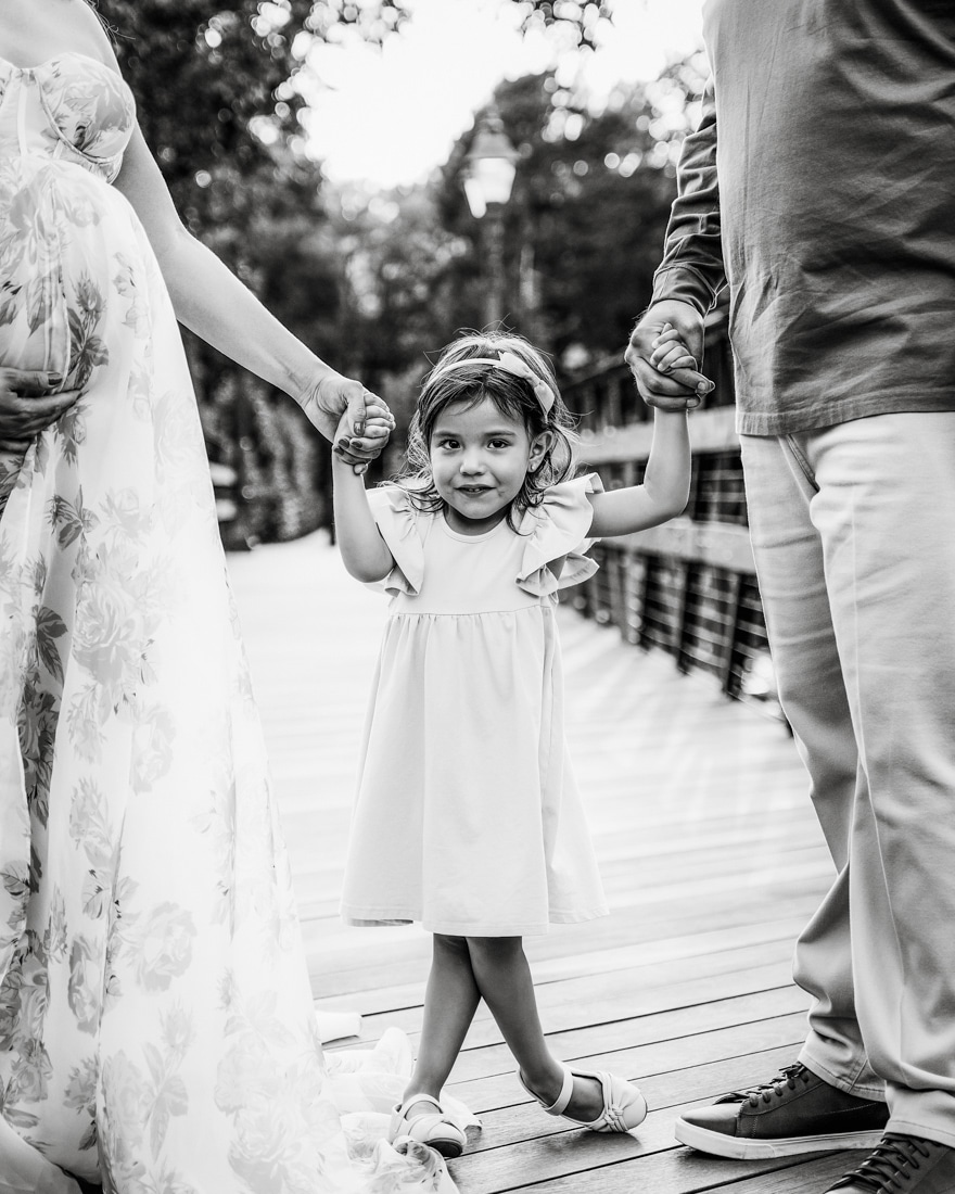 Close Up Photo Of Young Girl Holding Hands With Parents During A Pregnancy Photoshoot