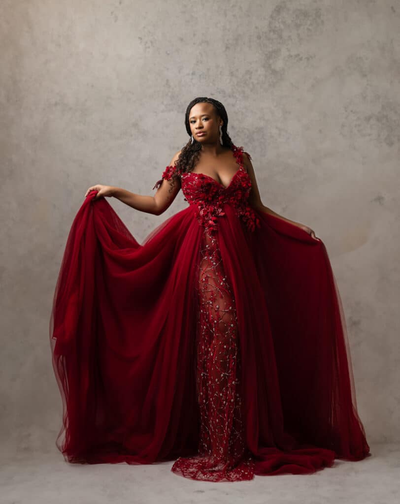 Woman In An Elegant Red Gown With Floral Details Posing For A Maternity Shoot Dallas