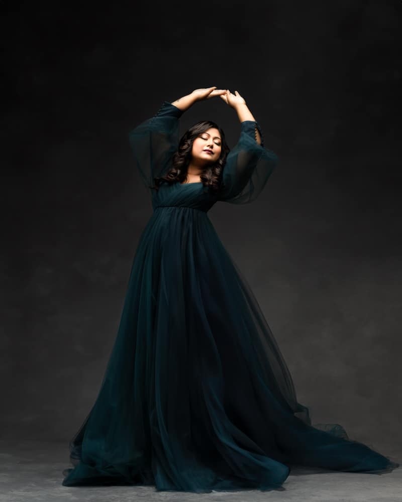 Woman In A Dark Green Gown Poses Gracefully With Arms Raised For Maternity Shoot Dallas