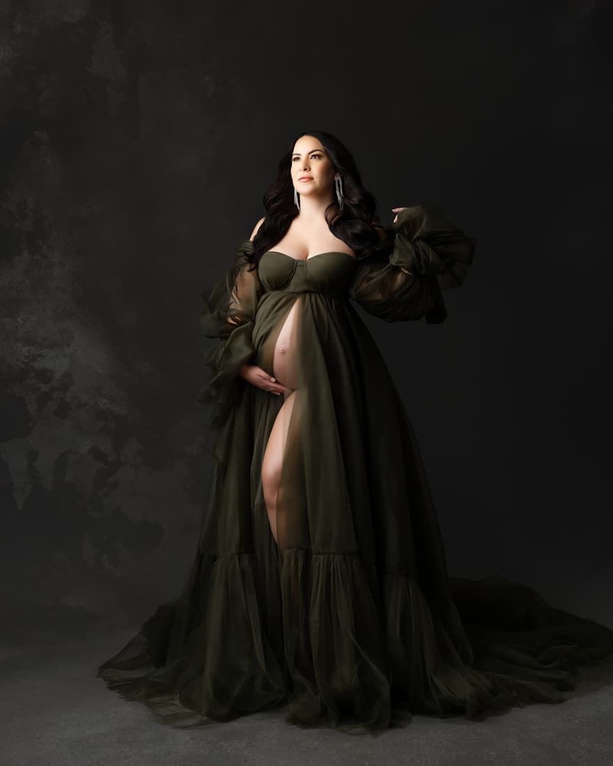 Pregnant Woman In A Flowing Gown Poses Against A Dark Background For Indoor Maternity Photoshoot Dallas