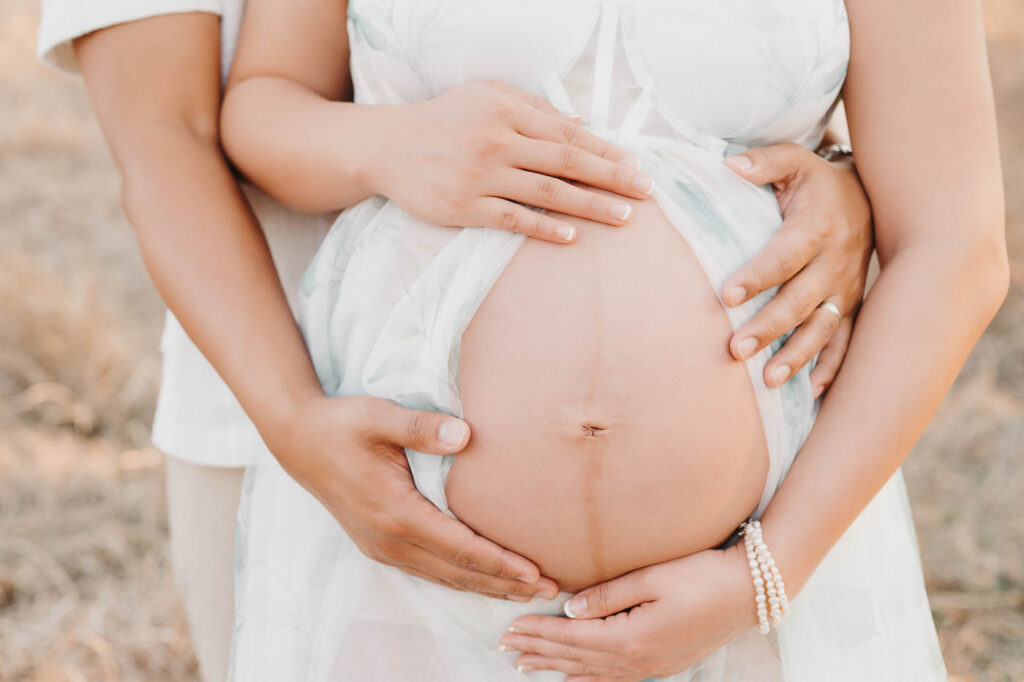Close-Up Outdoor Maternity Portrait Highlighting Baby Bump And Hands During Golden Hour Session