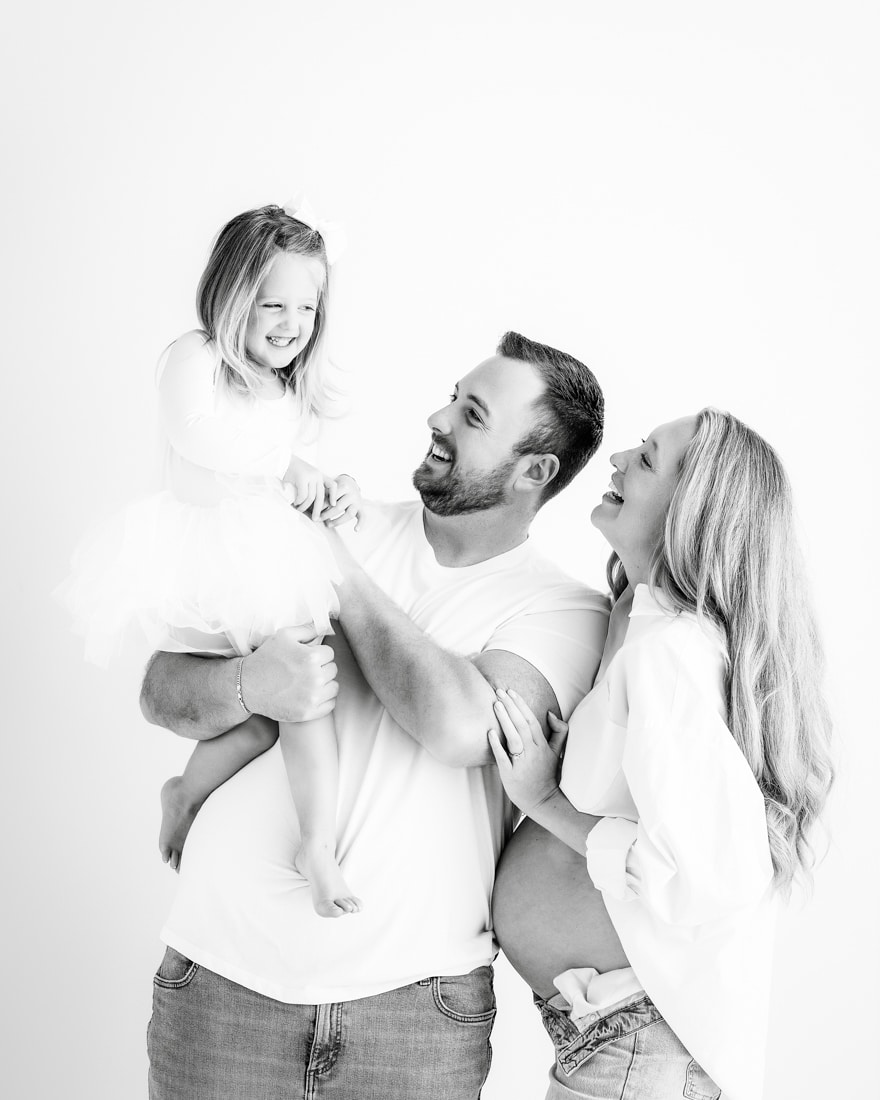 Man Holding A Smiling Young Girl While A Pregnant Woman Stands Beside Them, For Lifestyle Maternity Photos Dallas