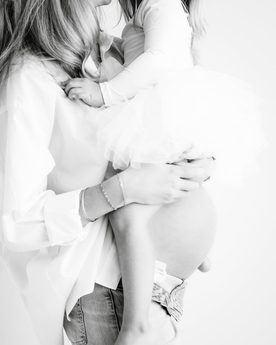 Pregnant Woman Holds A Small Child Dressed In A Tutu On Her Hip Both Smiling For Maternity Photography Dallas