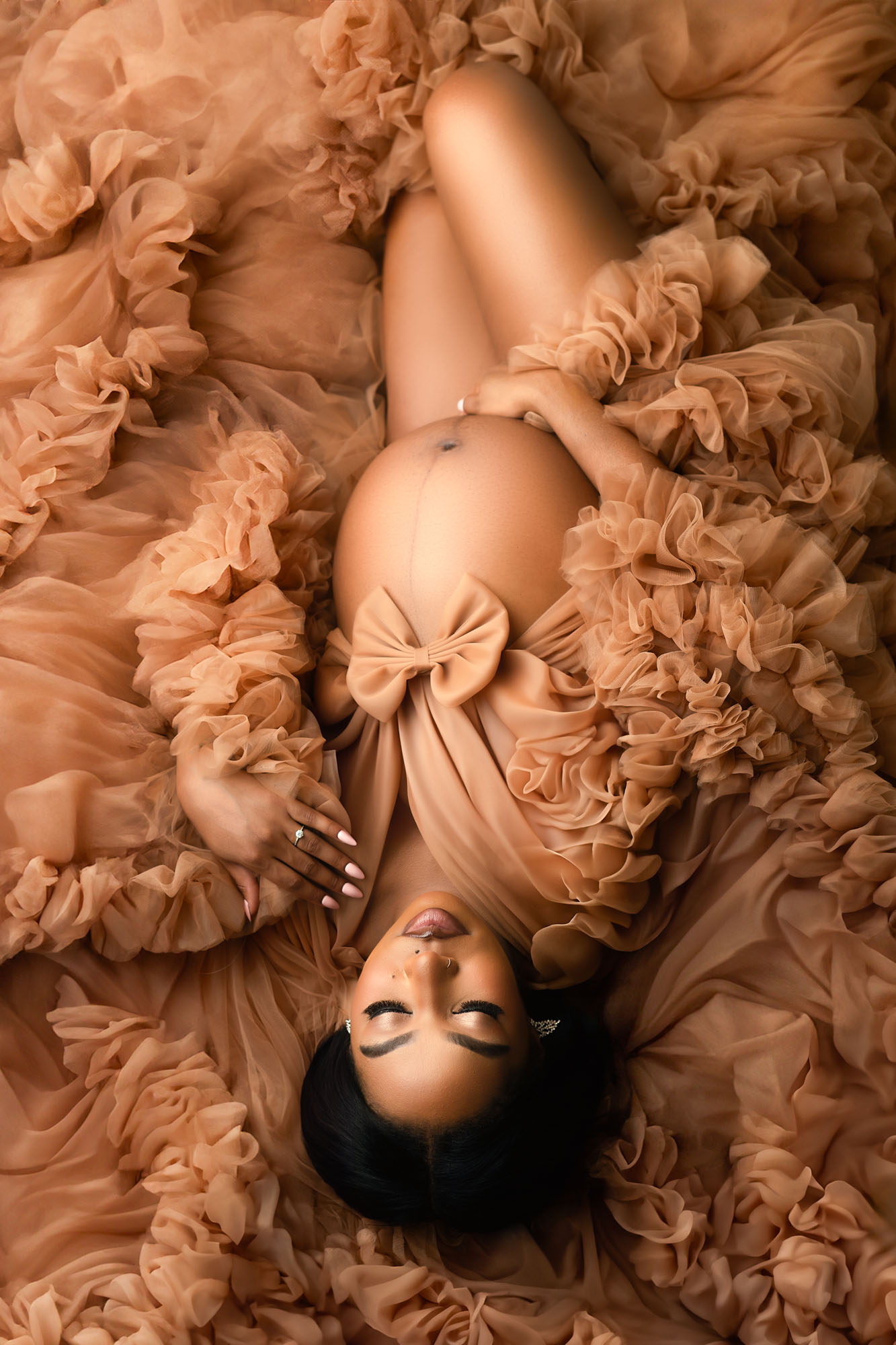 Pregnant woman in flowing brown gown with bow detail, elegant maternity photoshoot in Dallas