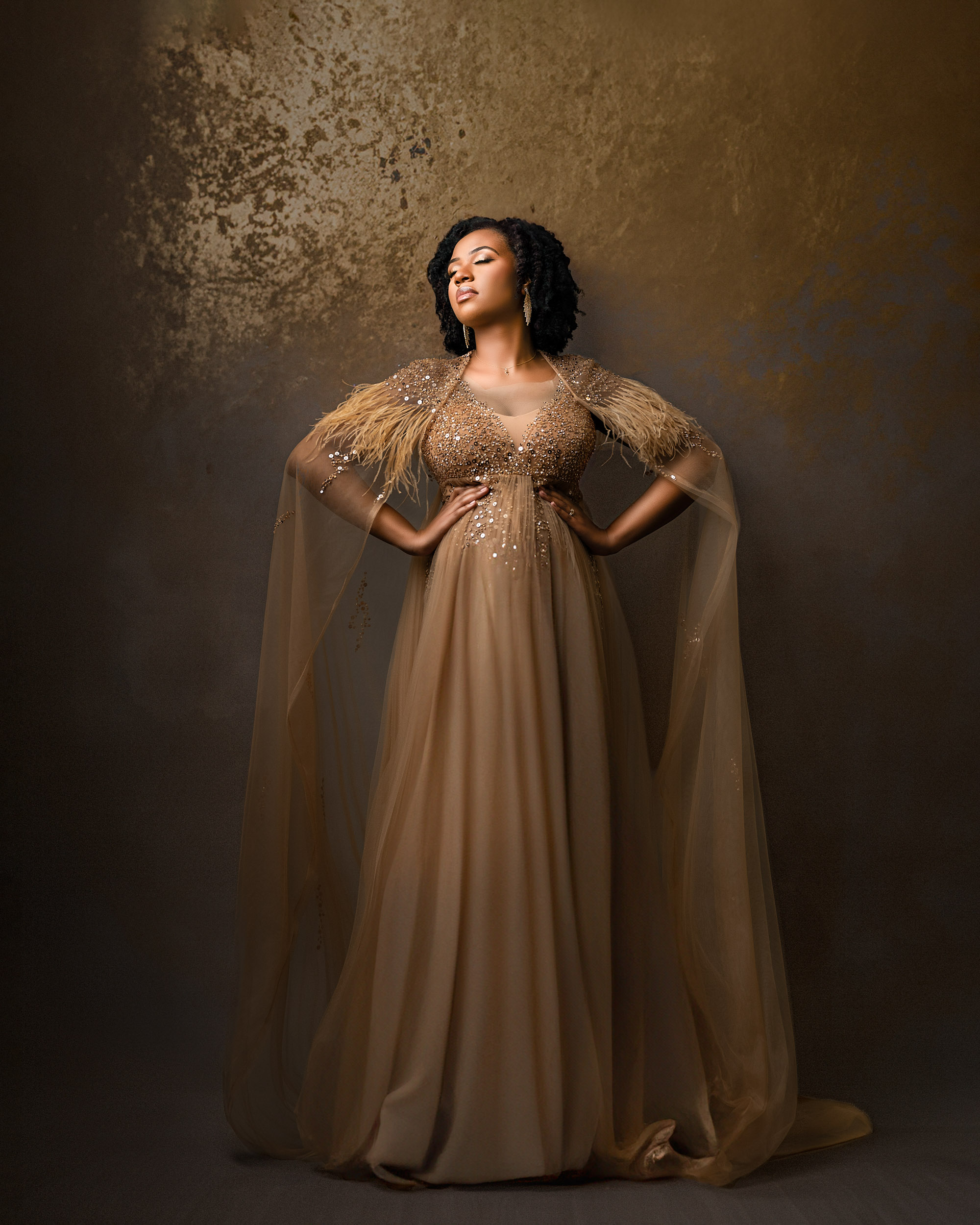 Luxury Maternity Portrait Of A Pregnant Woman In An Elegant Golden Gown With Feathered Sleeves, Standing Confidently Against A Warm Textured Backdrop, Captured By A Dallas Maternity Photographer