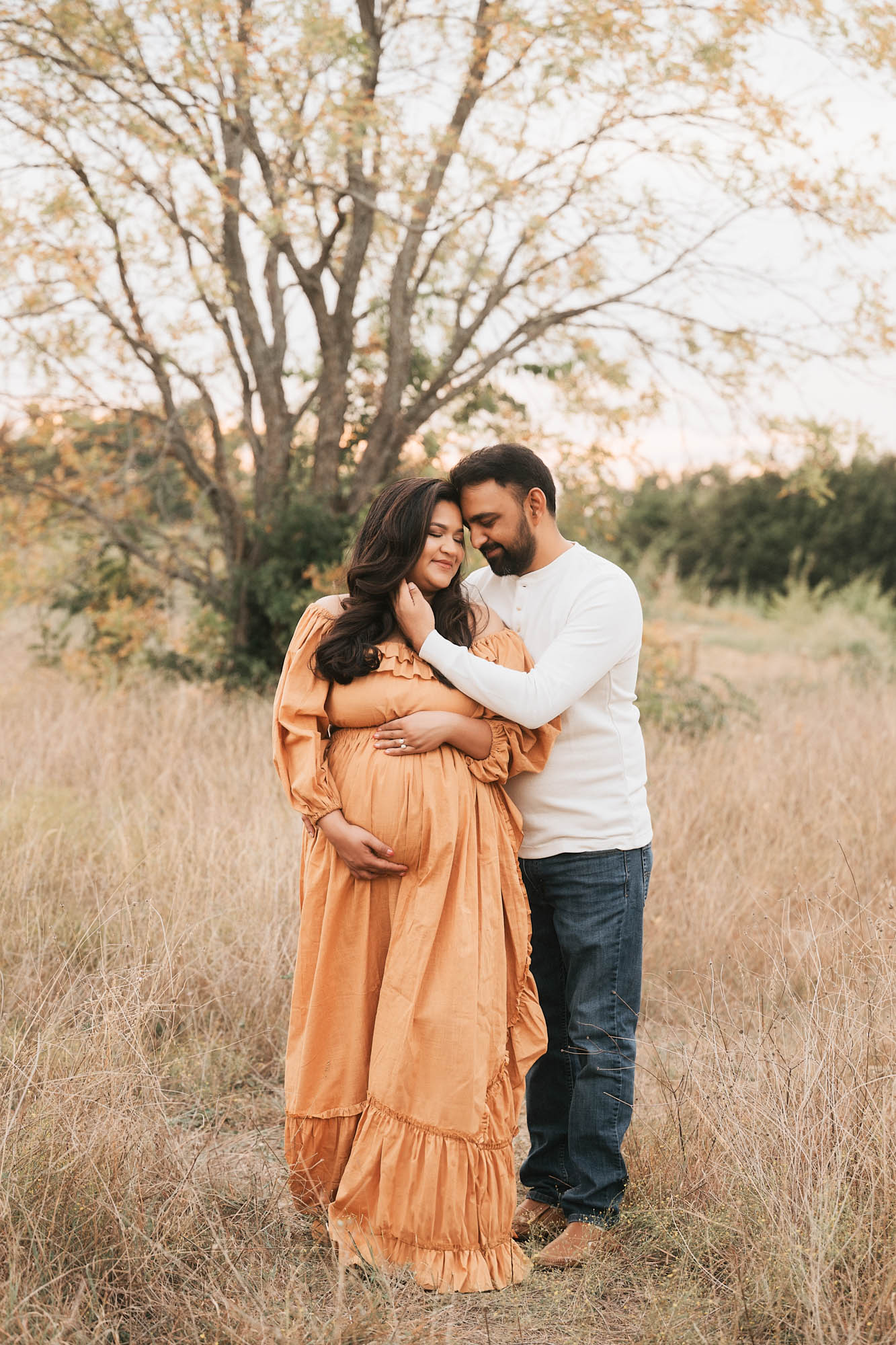 Expecting Couple Embracing In An Outdoor Dallas Field During A Warm, Golden Pregancy Photoshoot