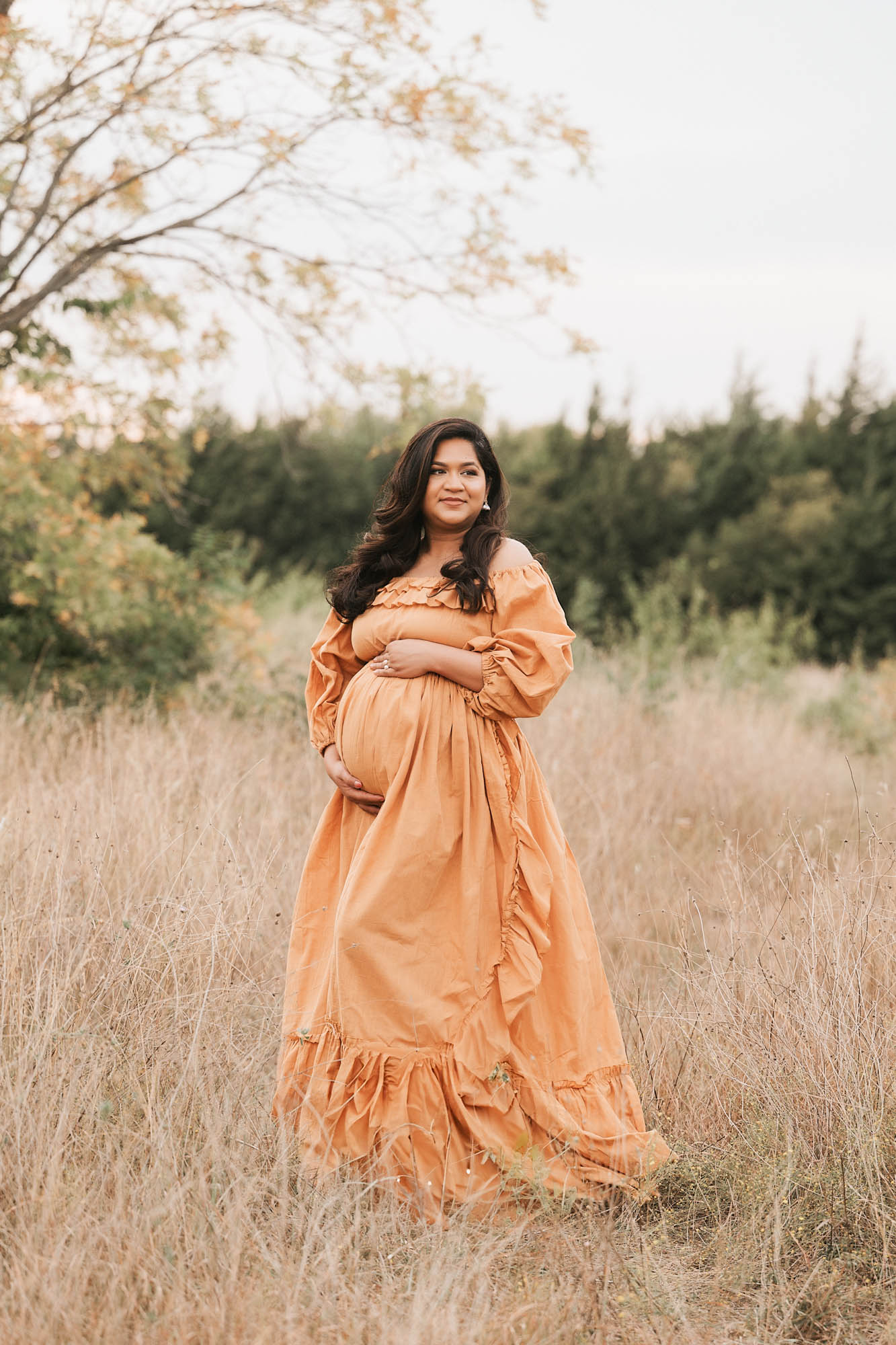 Pregnant Mother In A Mustard Gown Standing In A Golden Dallas Field During Sunset Maternity Session