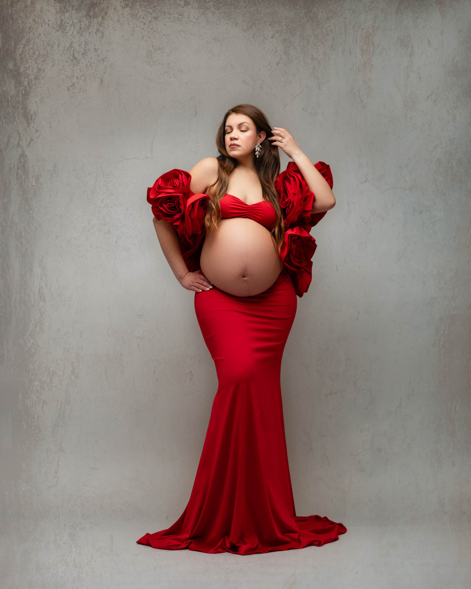 Dallas maternity photographer capturing an elegant studio pregnancy portrait of an expecting mother in a red couture gown