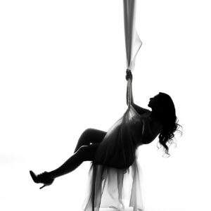 Artistic maternity photoshoot in Dallas featuring a dramatic silhouette portrait of an expectant mother suspended in flowing fabric.