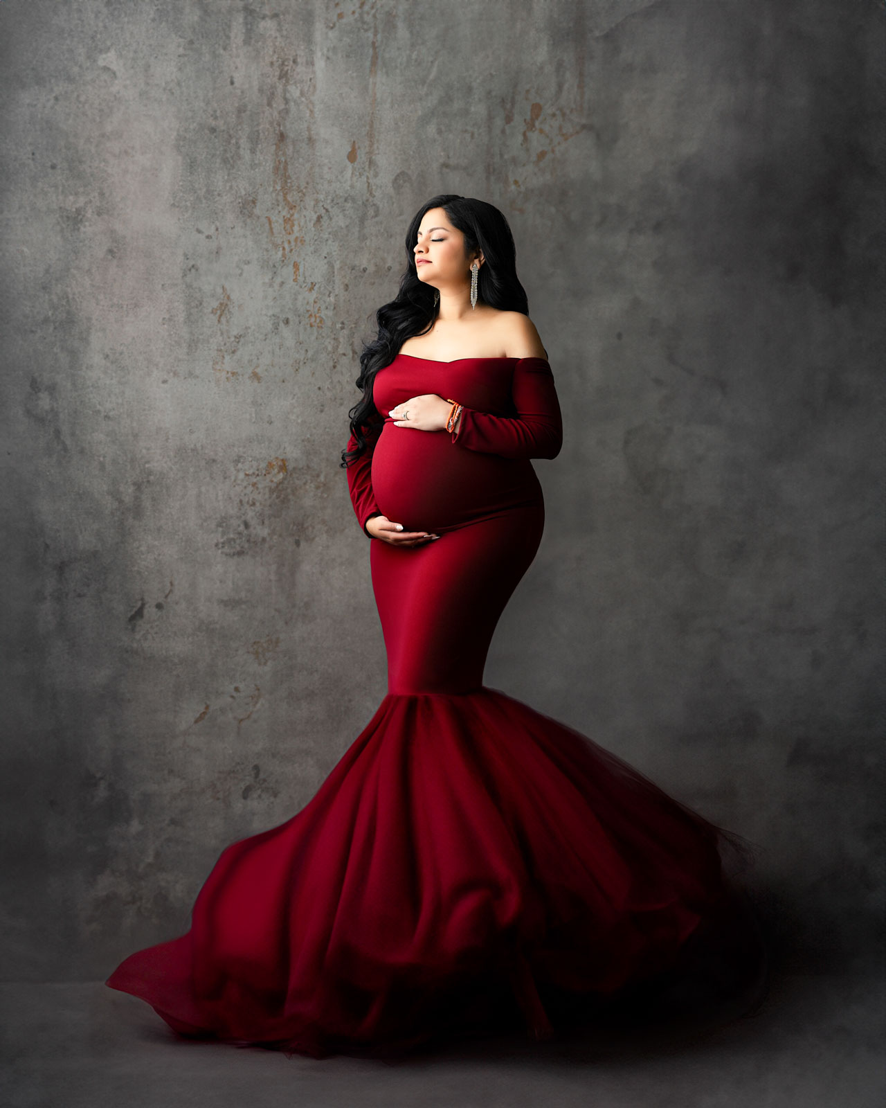 Fine art maternity photoshoot in Dallas featuring an expectant mother wearing a dramatic red gown in a luxury studio setting.