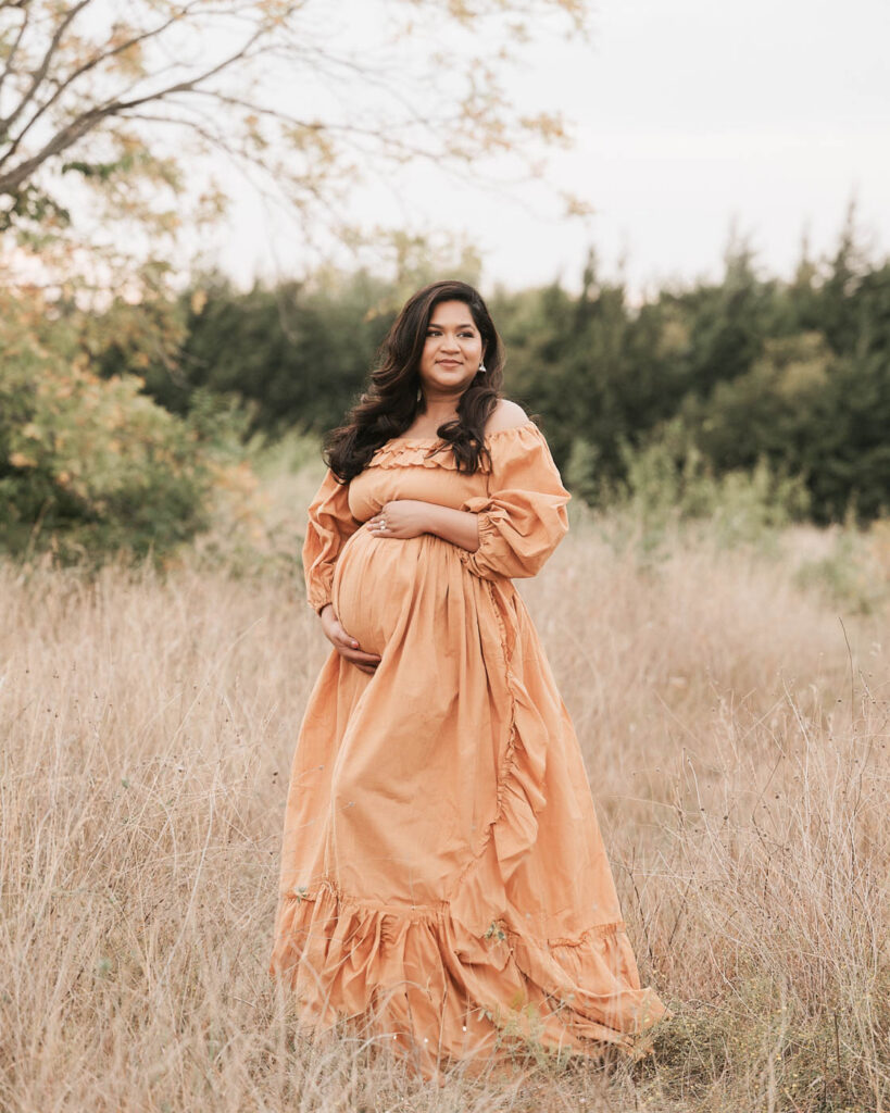 Pregnant Mother Standing In A Grassy Field During An Outdoor Maternity Photography Session In Dallas.