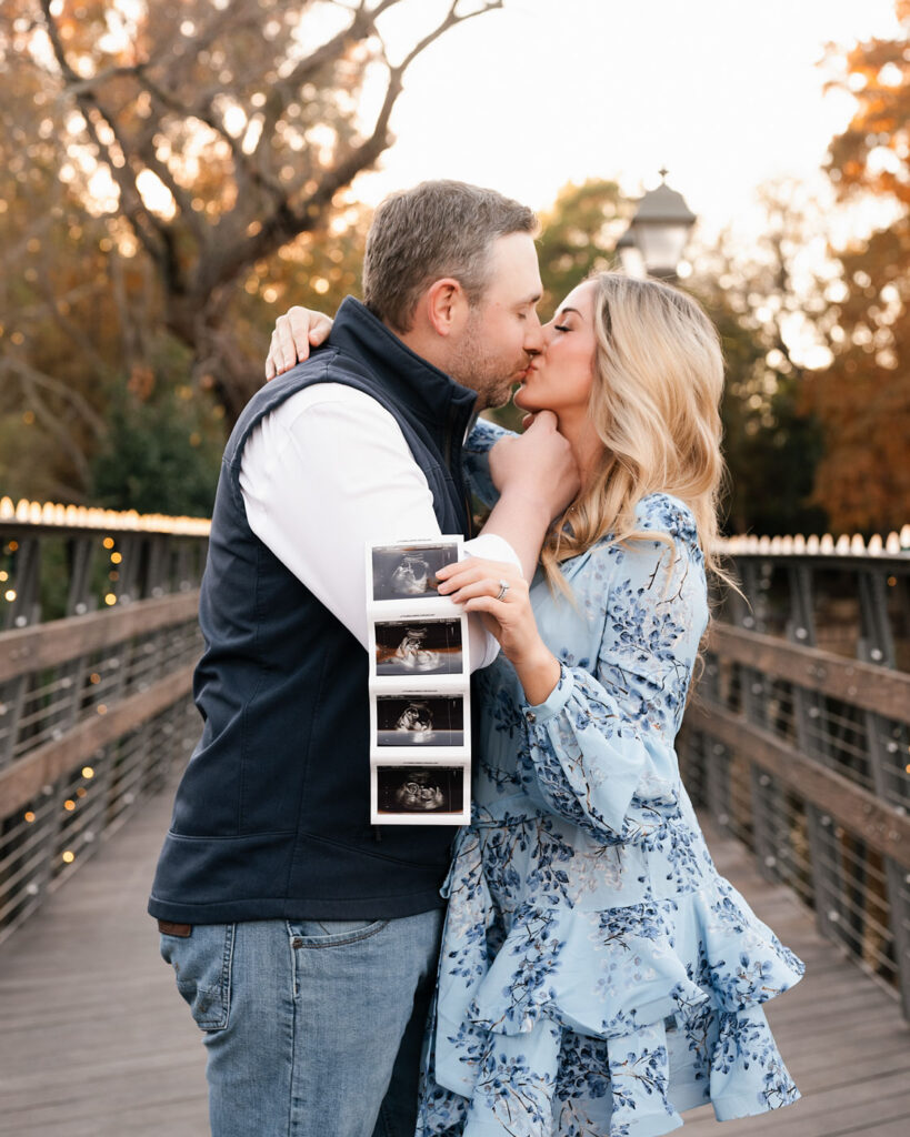 Couple Sharing A Kiss While Holding Ultrasound Photos During An Outdoor Maternity Session In Dallas Texas.