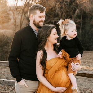 Outdoor family maternity portrait by a maternity photographer in Dallas featuring expectant parents and their young daughter during a sunset session.