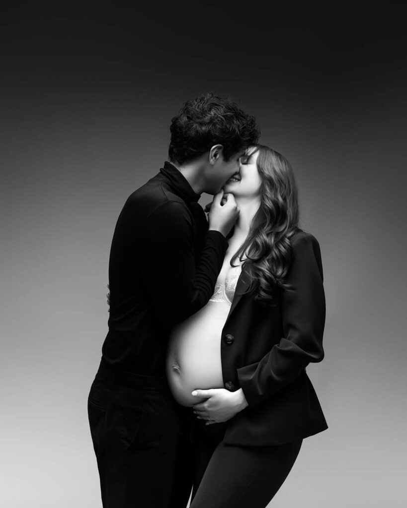 Maternity Photographer In Dallas Photographs An Expectant Mother In A Black Blazer Kissing Her Partner