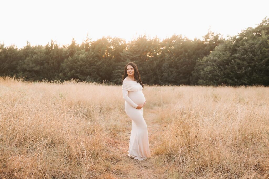 Wide Outdoor Maternity Portrait Of An Expecting Mother Standing In A Dallas Field During A Summer Evening Session.