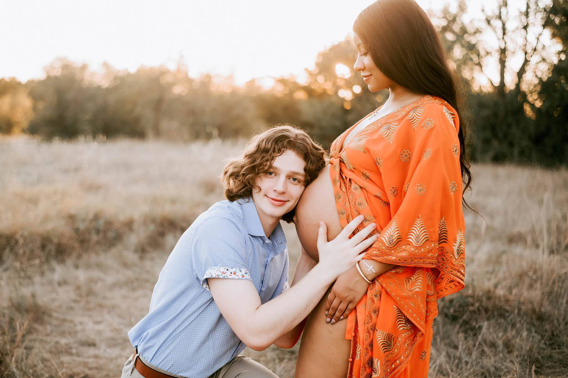 couple walks hand in hand through a grassy field smiling at camera for pregnancy photographer dallas