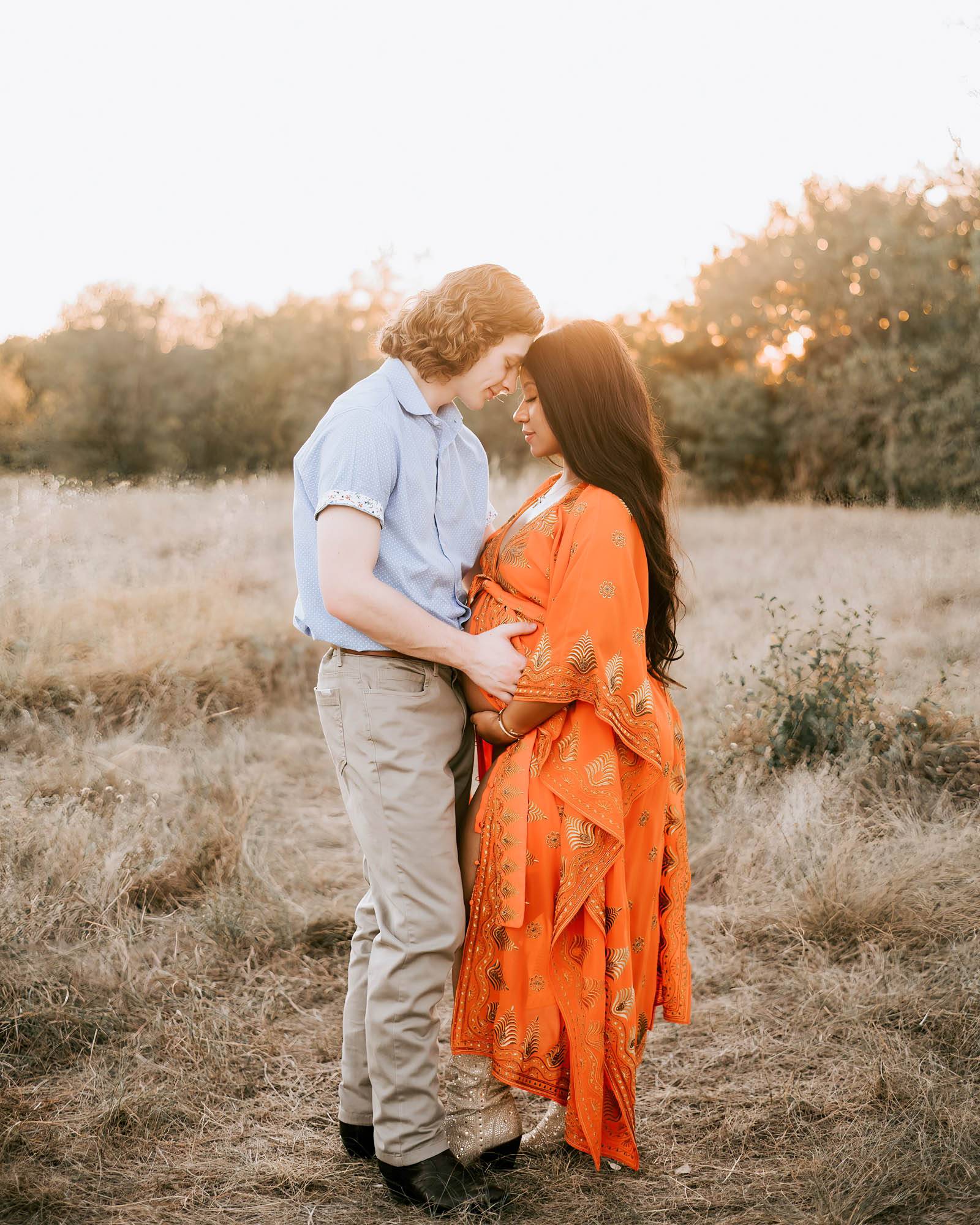 couple walks hand in hand through a grassy field smiling at camera for pregnancy photographer dallas